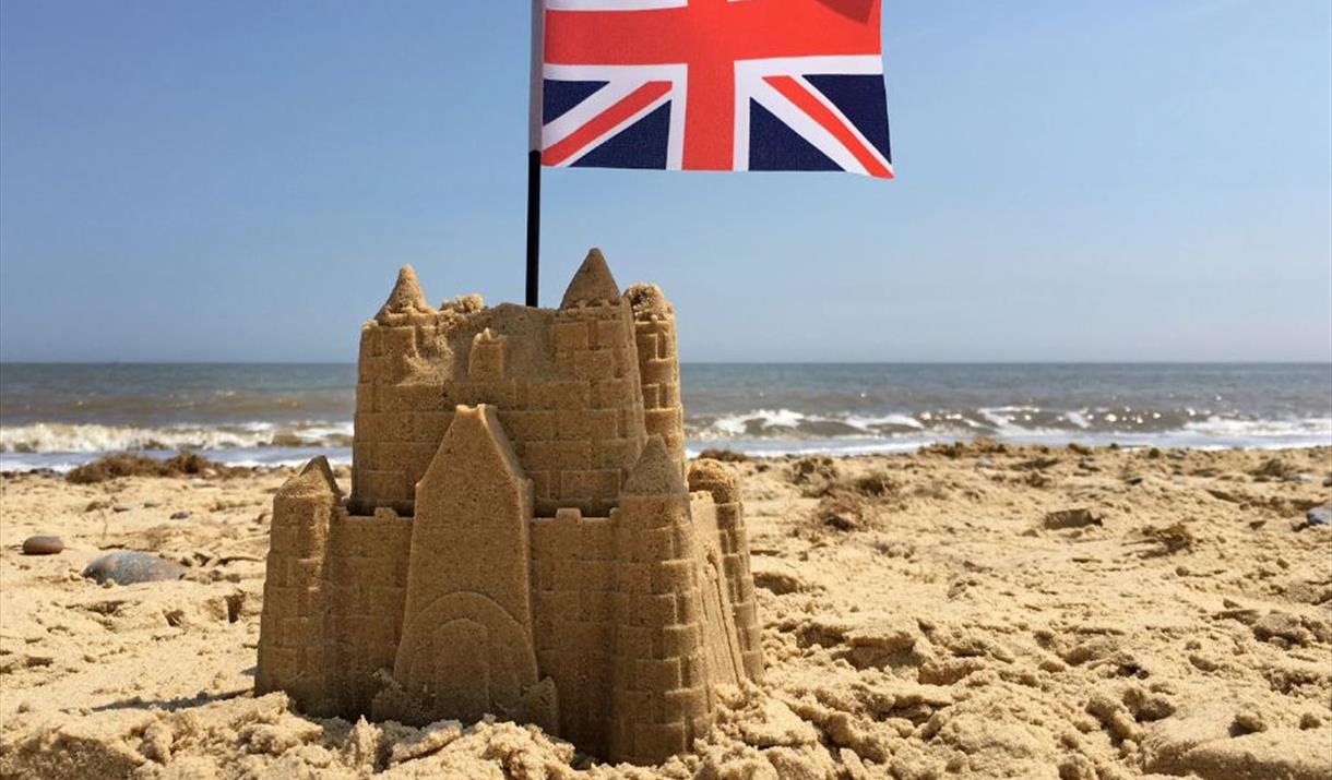 Sandcastle on a beach with a Union Jack flag on top