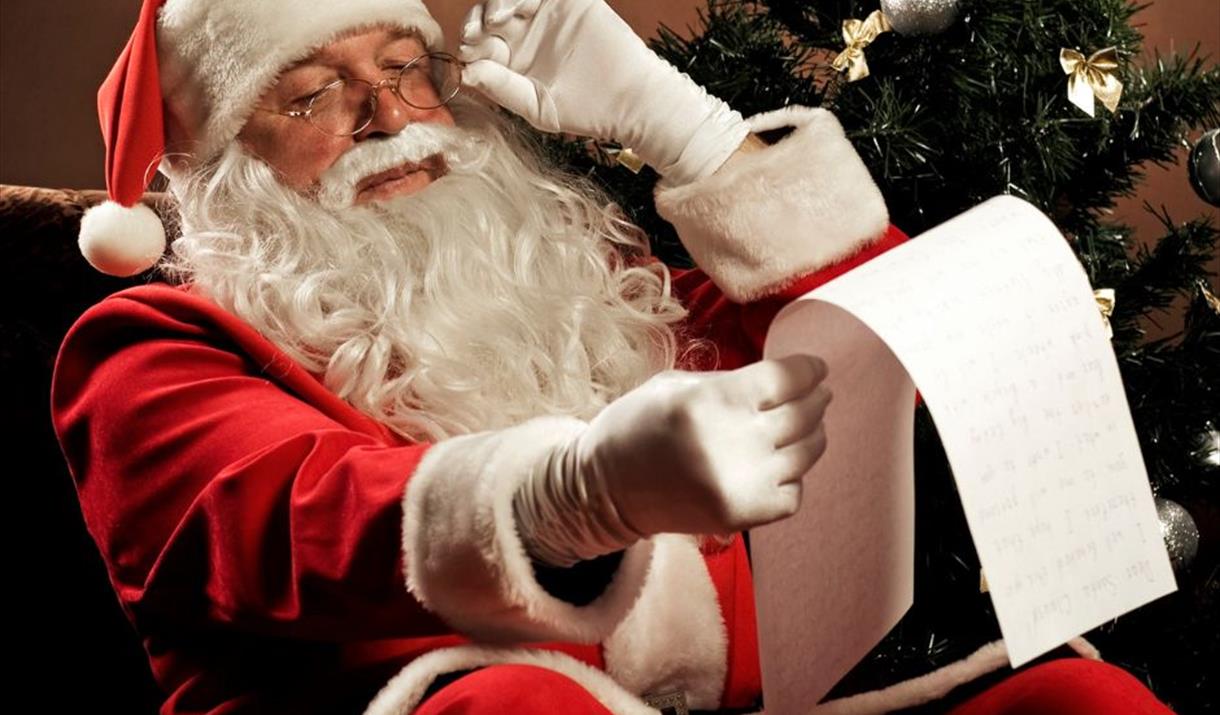 Santa Claus in his full red and white costume looking at a Christmas list