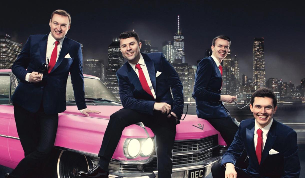 Oh What a Night singers sitting on a bright pink cadillac.