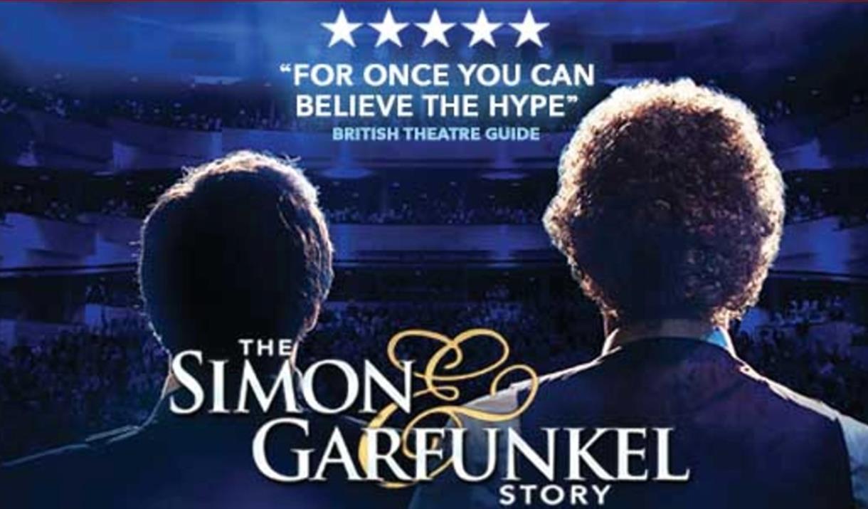 Two men standing away from the camera facing into the audience with spot lights on them.