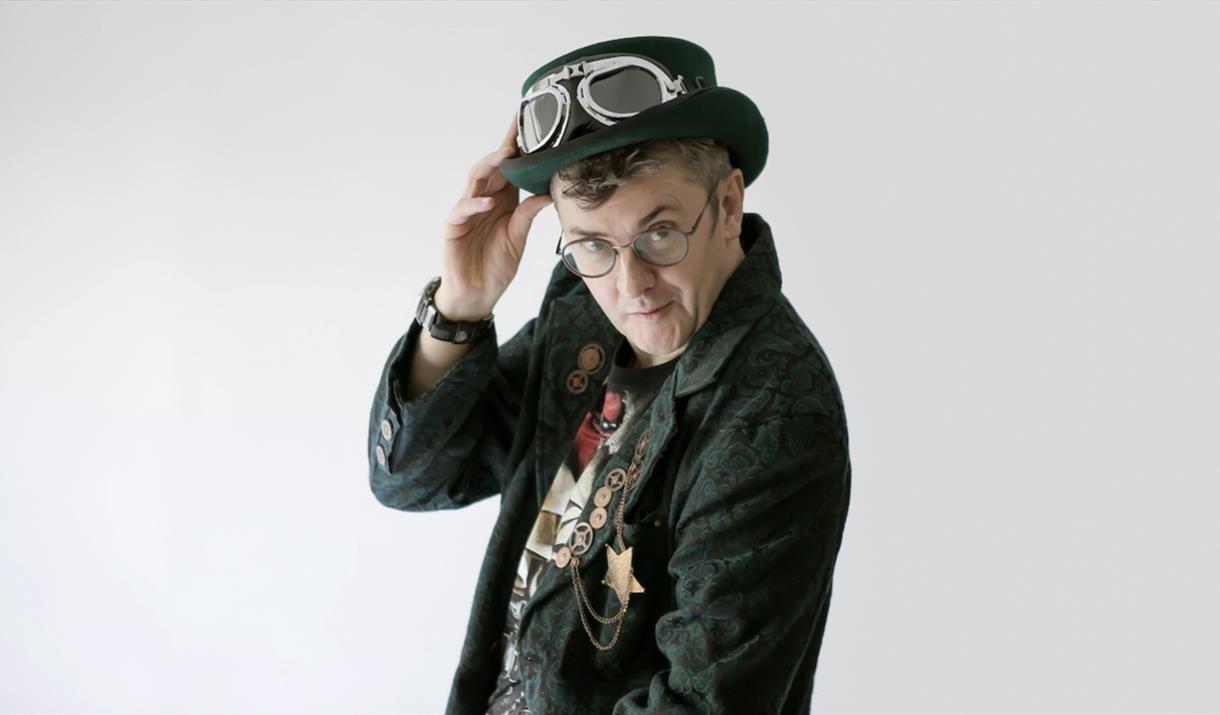 Joe Pasquale staing at the camera with a green suit and a light grey background.