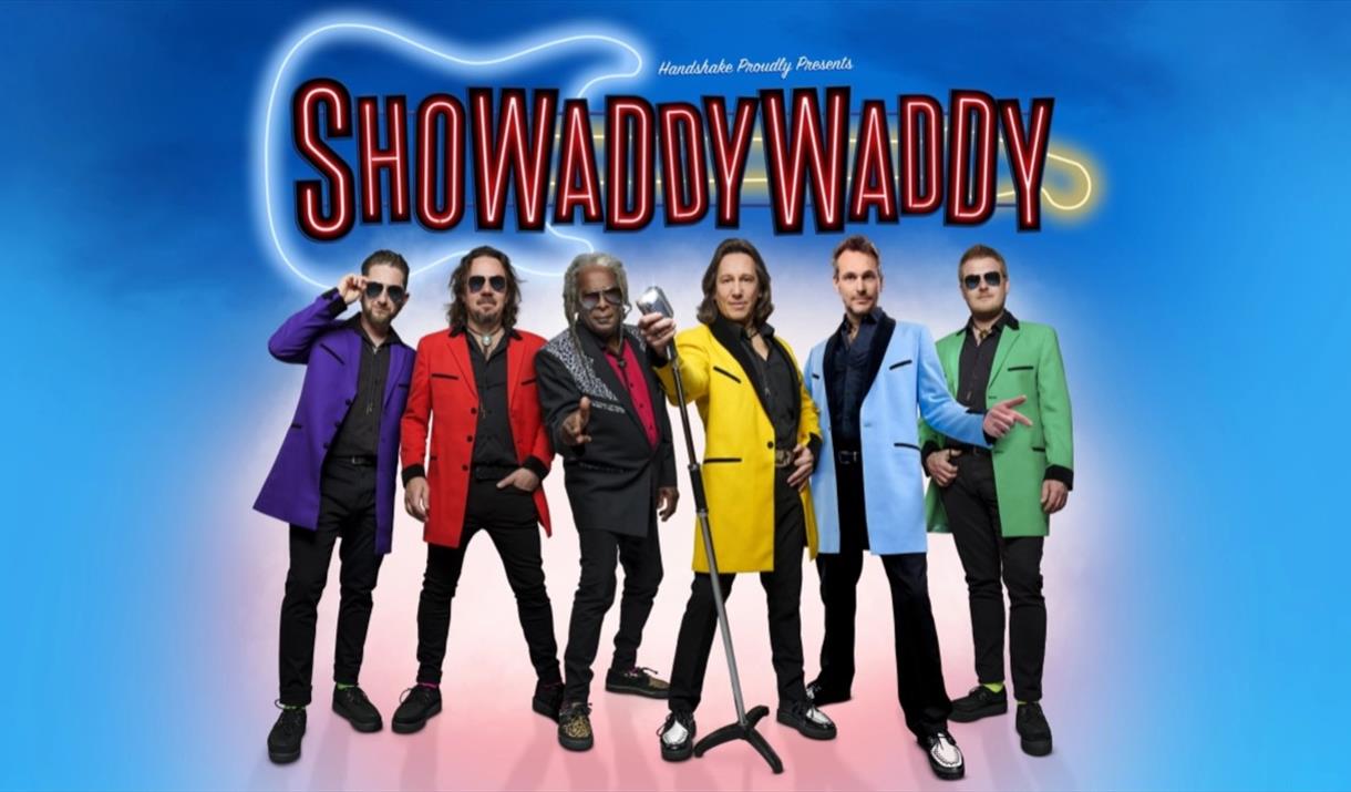 Six members of band Showaddywaddy in colourful suits standing around one microphone