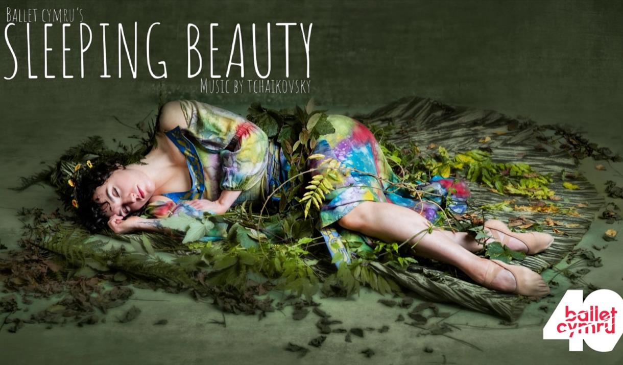 A ballet dancer lying on a green surface covered in leaves and flowers