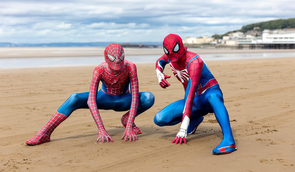 Two characters dressed as Spiderman in a crouched down Spiderman pose on Weston-super-Mare beach