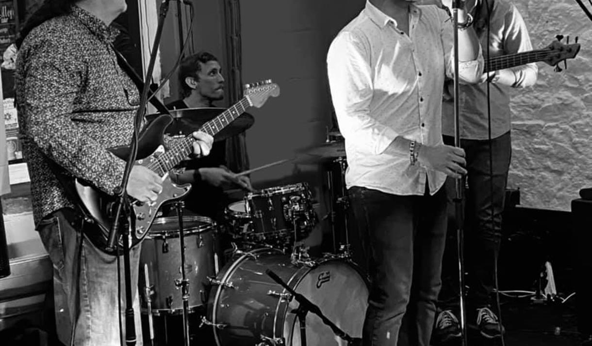 Black and white picture of three band members performing in front of their seated drummer