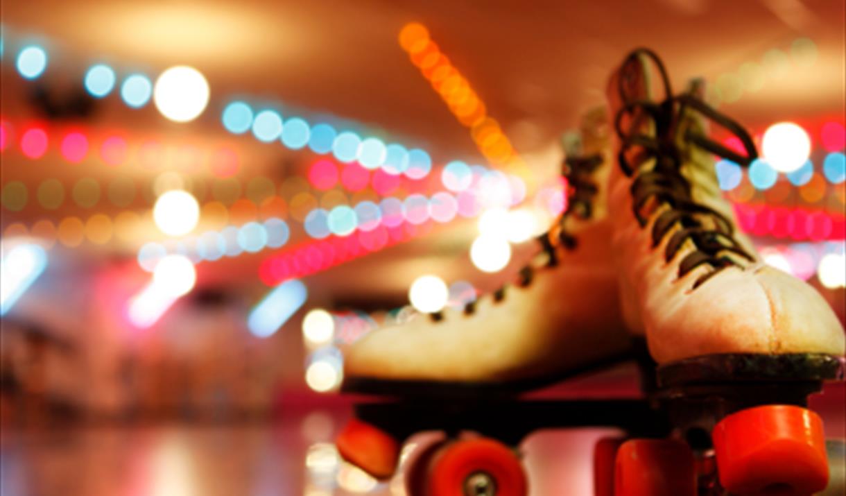 White roller boots with red wheels on a wooden floor.
Bright disco lights in the background.