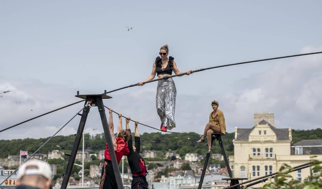 A trapeze artist walking on a tightrope and holding a large pole for balance
