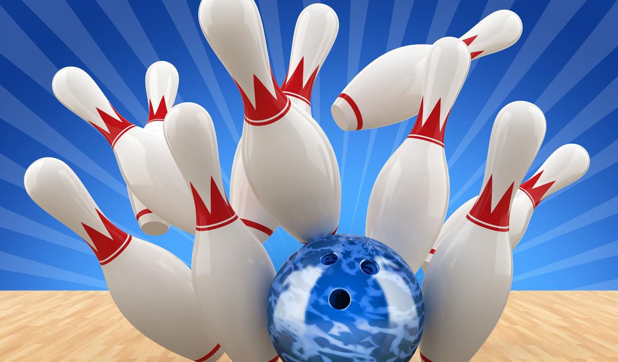 A blue bowling ball sending the pins flying at the end of a wooden bowling alley