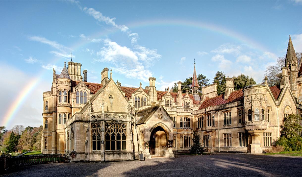 Exterior view of a large turreted mansion with a rainbow above