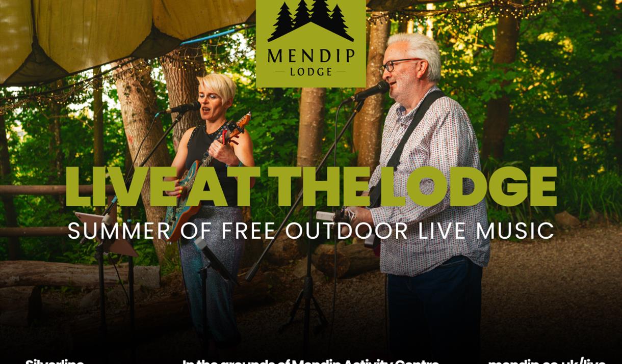 Two musicians (man and woman) playing guitar and singing into microphone under tented woodland canopy. Woodland trees in background. Mendip Lodge logo