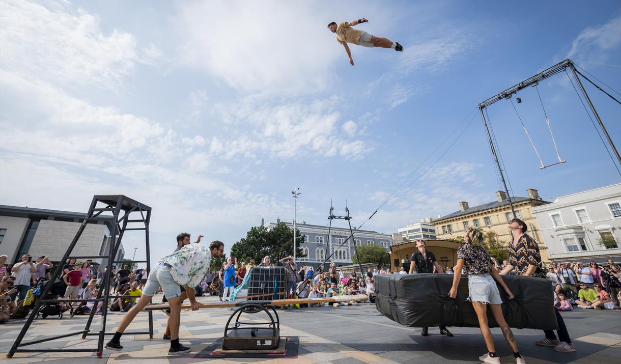 An acrobat high in the blue sky above the crowds and some apparatus