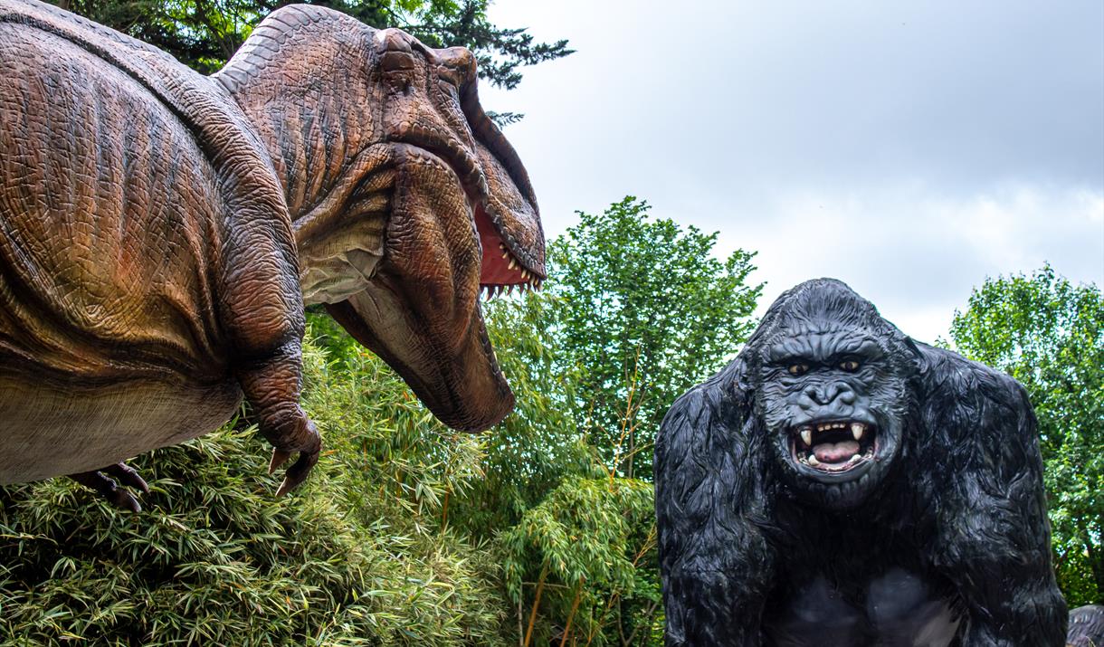 An animatronic dinosaur at Wookey Hole staring at a giant model gorilla