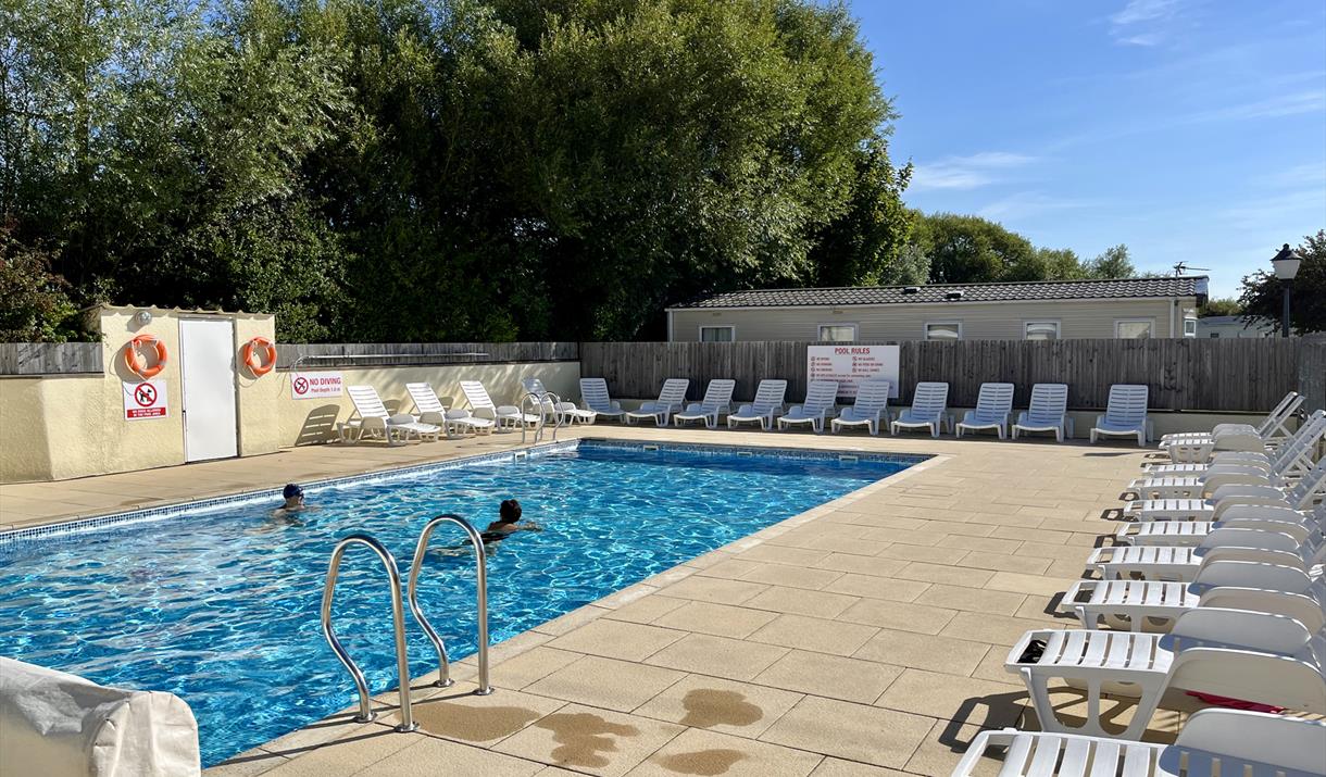 Outdoor swimming pool on a sunny day with two people swimming and lots of empty sun loungers