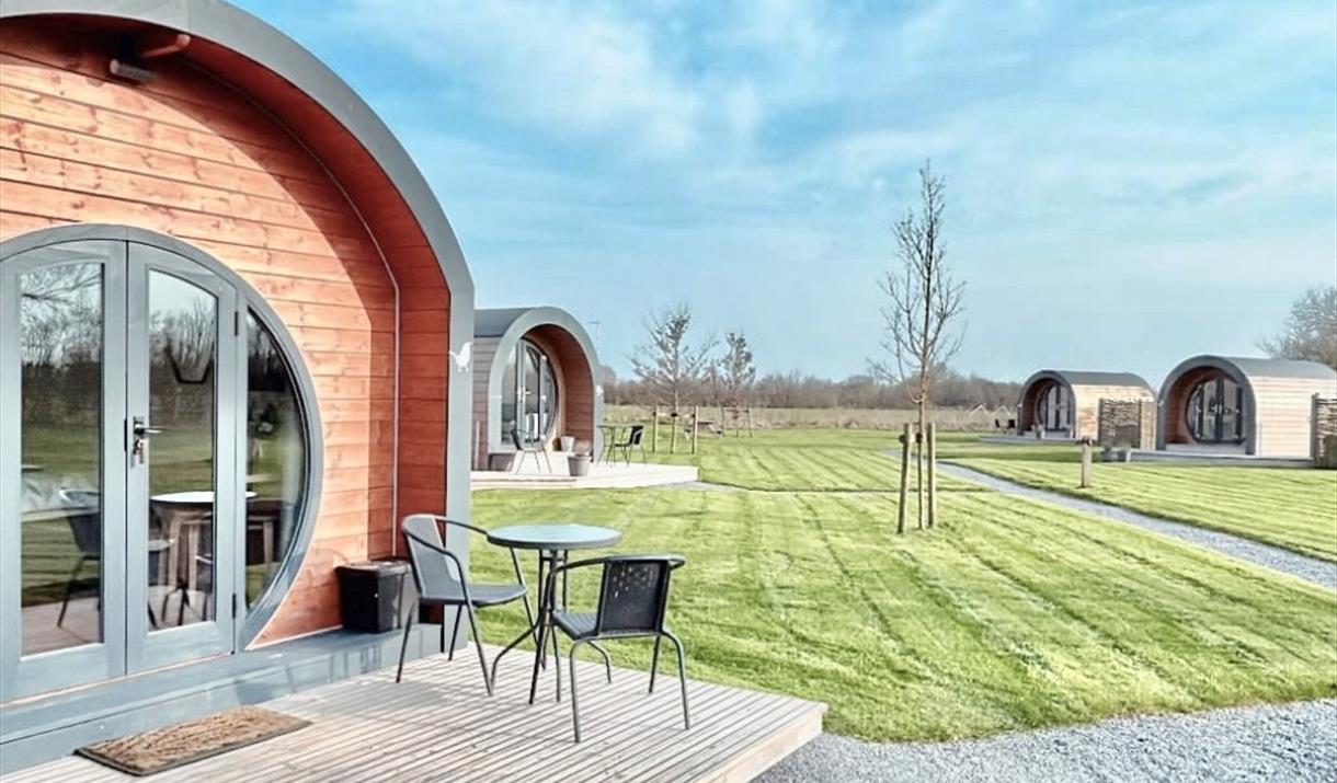 Entrance to a luxury glamping pod with seats on the decking and other pods in the background