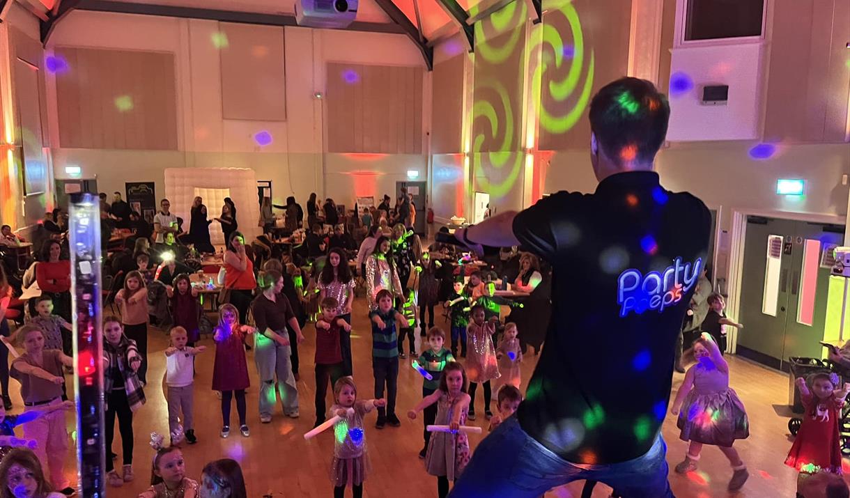 The back of a performer on stage entertaining a crowd of young children and families on a dancefloor