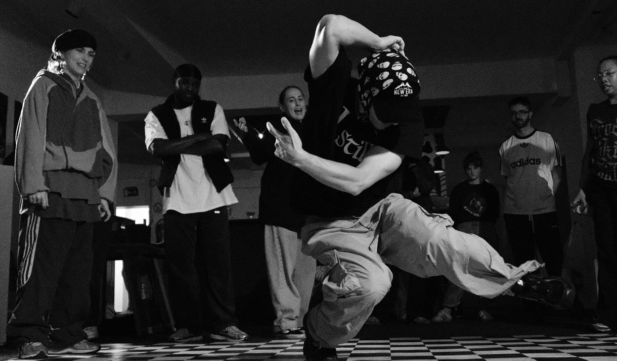 Black and white photo of man breakdancing on chess board floor