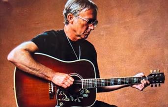 Guitarist Steve Craddock dressed all in black sitting down and playing his guitar
