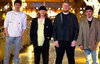 Four members of the Instigators Band standing in a shopping centre with Christmas lights behind them