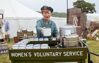 A women in WRVS uniform serving mugs of tea at a Women's Voluntary Service tea stand at a 1940s weekend