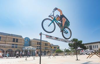 Mountain Bike Stunt Rider Rich Pearson jumps over a high bar challenge in the Italian Gardens Weston-super-Mare
