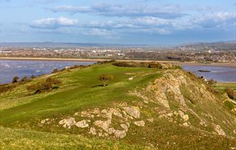 View over the top of a grass-topped rocky cliff with sea on either side and a shoreline in the background