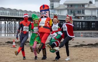 Four runners in festive fancy dress put their best foot forward on the beach in front of the Grand Pier, Weston-super-Mare ahead of the town's annual