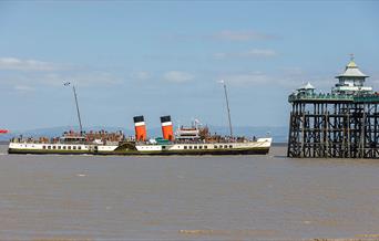 A paddle steamer passing by the end of a pier