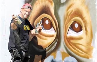 A street artist with spray can working on a giant mural of a monkey