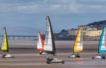 Five Blokarts with their colourful high sails racing across a sandy beach
