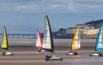 Five Blokarts with their colourful high sails racing across the sandy beach at Weston-super-Mare