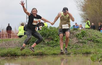 Two competitors in an endurance race jump together above a water pit