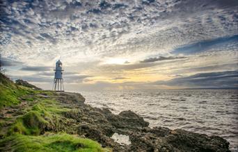 A distinctive lighthouse sitting on rocks beneath a sunset
