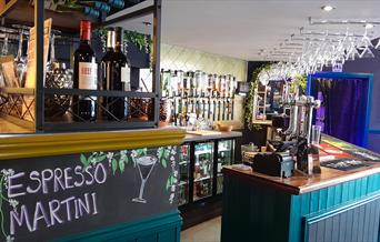 An empty bar with wine glasses hanging from the ceiling and wine bottles in the foreground