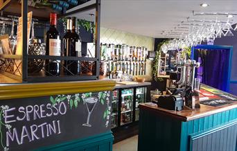 An empty bar with wine glasses hanging from the ceiling and wine bottles in the foreground