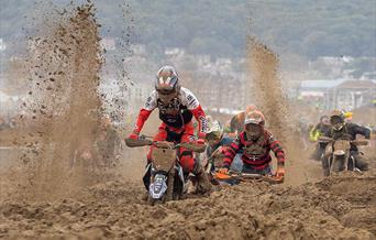 Sand flies up as three motorbike riders struggle through sand in a beach race