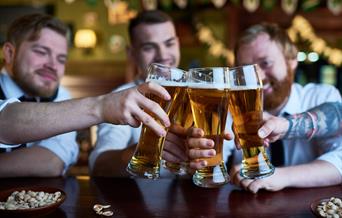 Three men in a pub clinking their full pint glasses