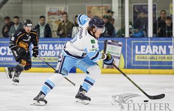 A Bristol Pitbulls ice hockey player in their light blue and white kit comes away with the puck