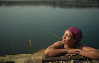 Woman in swimcap, arms drapped over pool edge, looking happy