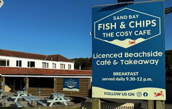 Close up image of the Sand Bay Fish & Chip shop sign against a blue sky with the premises in the background