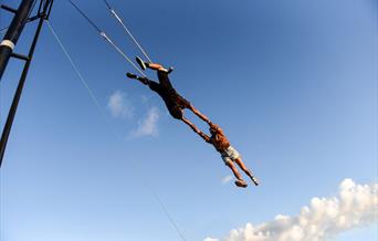2 people on a trapeze, flying through the blue sky