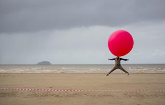 A man on the beach with a giant balloon over his head.