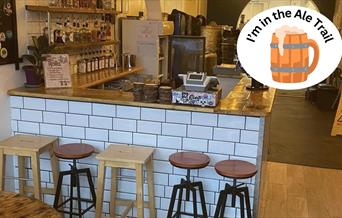 An empty bar counter with white tiles and five assorted stools in front of it