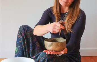 A person sat on the floor using a singing bowl. There are other bowls around them
