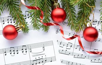 Red Christmas baubles and the branches of a Christmas tree overlaid on a sheet of music