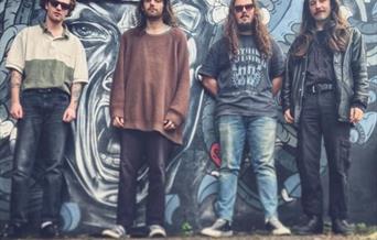 The Guzzlers poster with band members stood against a graffiti wall.