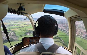 View from the back seat of a an airborne helicopter showing the pilot, cockpit and view