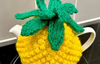 Photograph of a yellow hand-knitted tea cosy