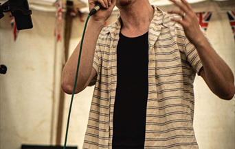 Photograph of James Anthony singing into a microphone on stage with event information.