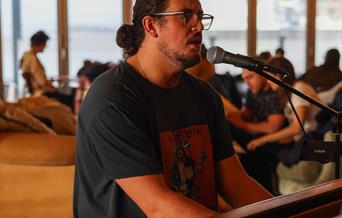 Photograph of Harrison singing into a microphone and playing a piano