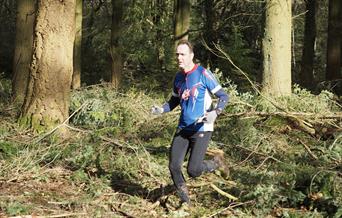 A man running in the woods wearing a blue, white and red running top